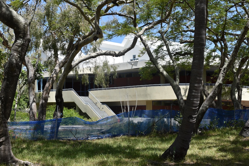 An old building with blue mesh fencing around it and trees