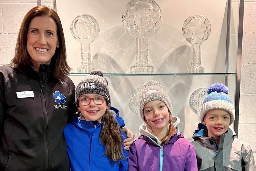 A woman and three children stand in front of a trophy case