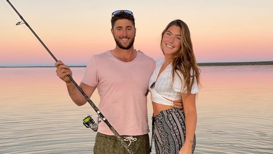 Man in shallow water at beach  holds a fishing rod with arm around waist of lady with long hair