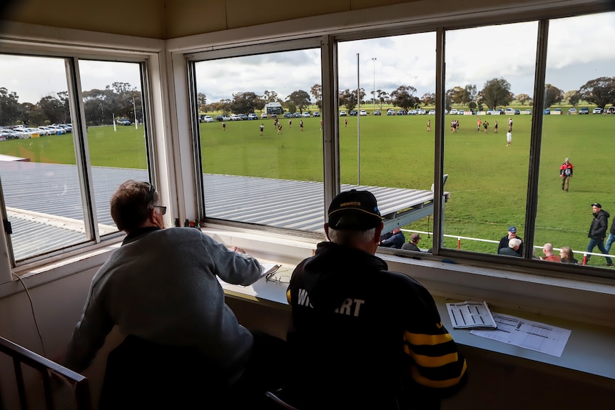 Two men sit in a box overlooking a football ground