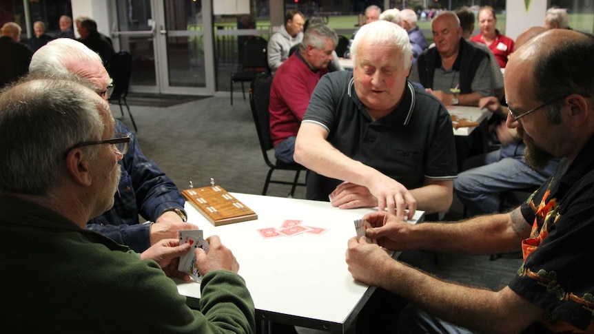 A group of men sitting around playing cribbage.