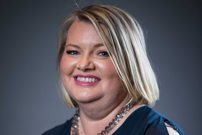 A woman with short blonde hair and a bright face smiles at the camera