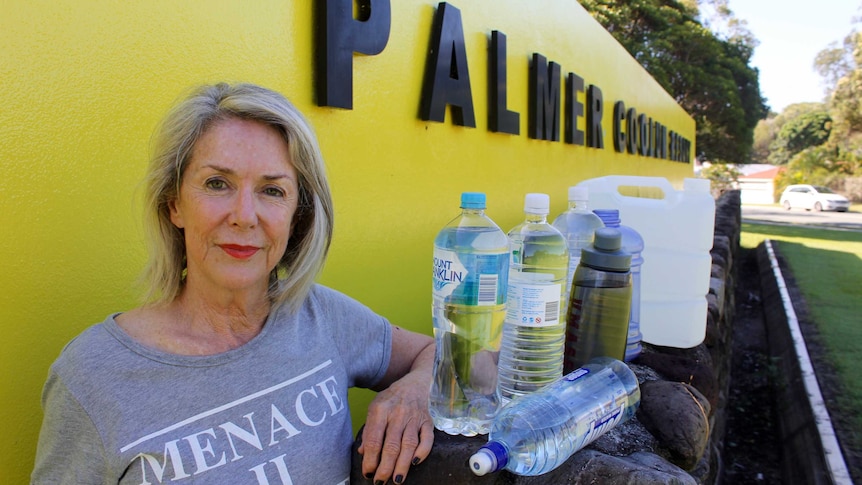 Woman stands beside yellow sign with water bottles
