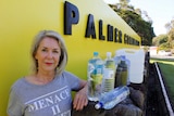 Woman stands beside yellow sign with water bottles