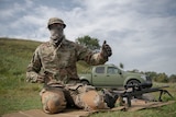 A sniper sits beside a rifle on a firing range