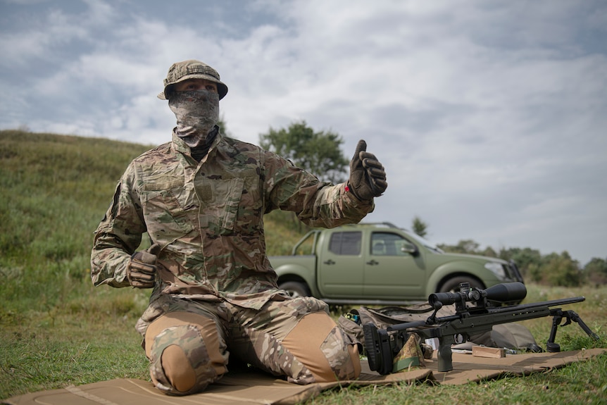 A sniper sits beside a rifle on a firing range