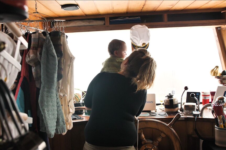 Maeve MacGregor with daughter at the helm of their live-on boat moored at Margate in Tasmania's south. July 2021.