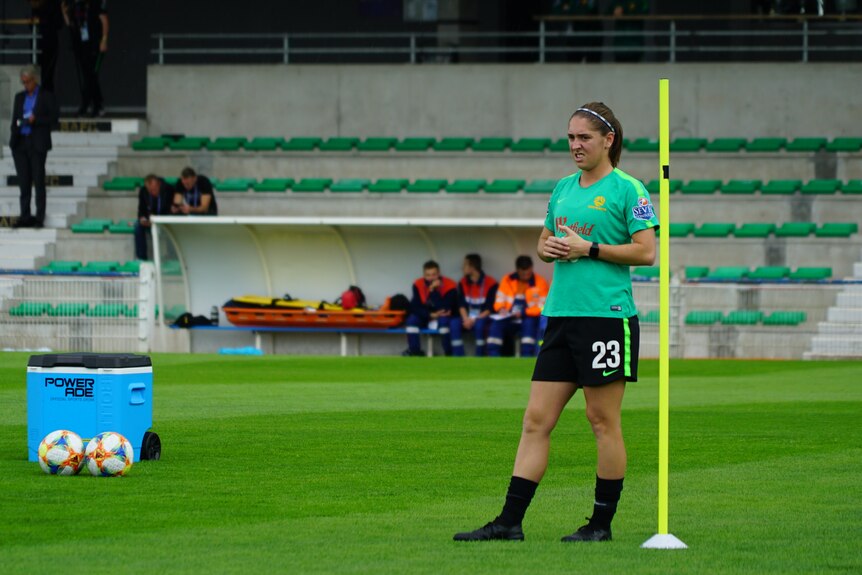 Karly Roestbakken stands next to a yellow training pole inside a football stadium.
