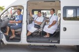 Three woman smile out of a white van with doors open.