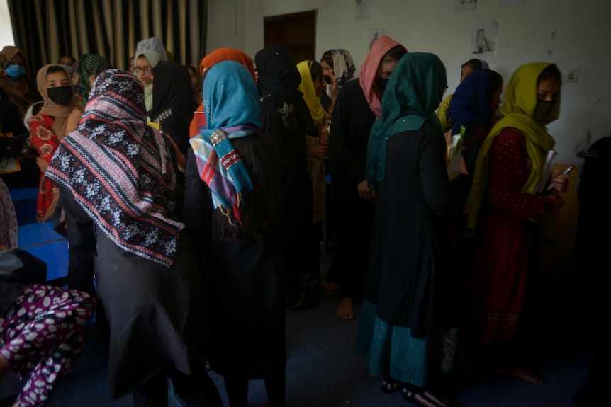 A group of young women line up in a room to enter class. 