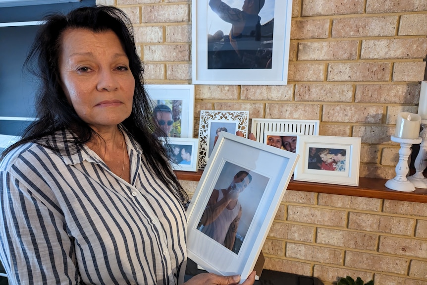 A woman stands with a framed picture of a young man