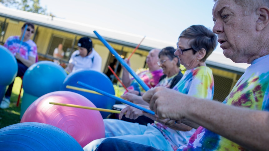 A group of people with a disability sit in a circle drumming on large exercise balls.