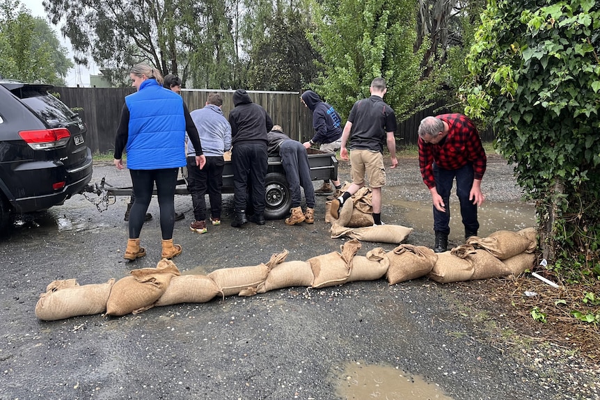 A group of people unload sandbags from a trailer onto the ground.