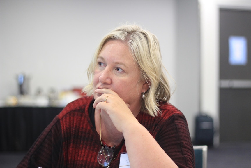 A woman with fair hair and skin, resting her chin on hand.