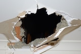 A circular hole appears to have been blasted through a white plaster ceiling, photographed from indoors.