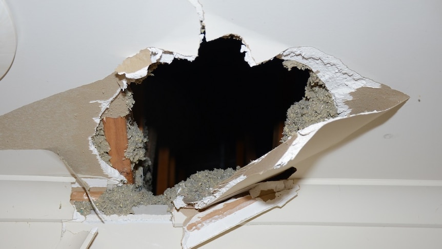 A circular hole appears to have been blasted through a white plaster ceiling, photographed from indoors.