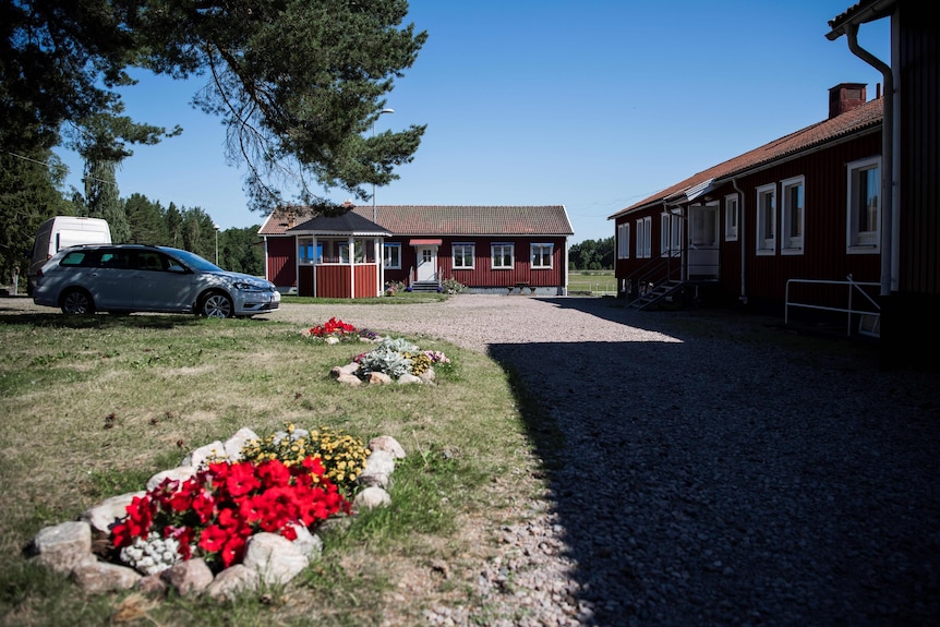 Red wooden houses and a garden, with farmland in the background.