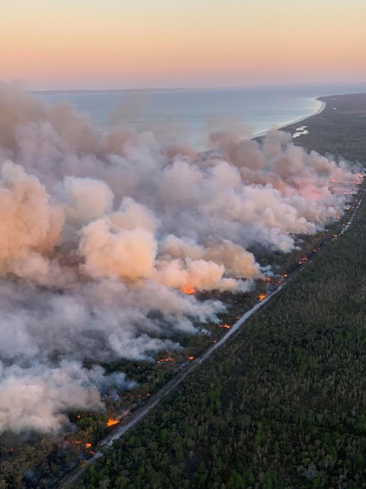 Aerial shot of smoke plumes rising from a coastal bushfire at dusk