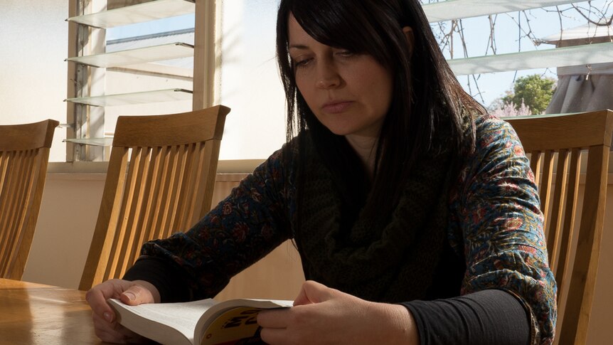 Kate Henderson sits and reads a book in her sunroom.