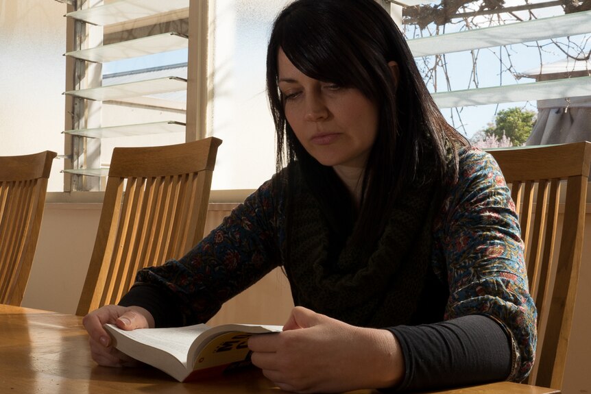Kate Henderson sits and reads a book in her sunroom.