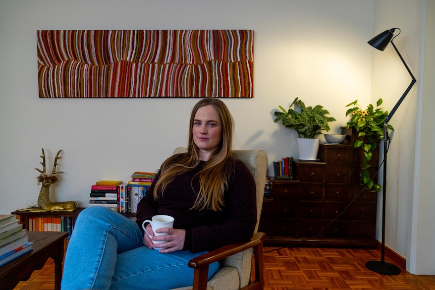 A woman wearing black sits surrounded by books, plants and a lamp.