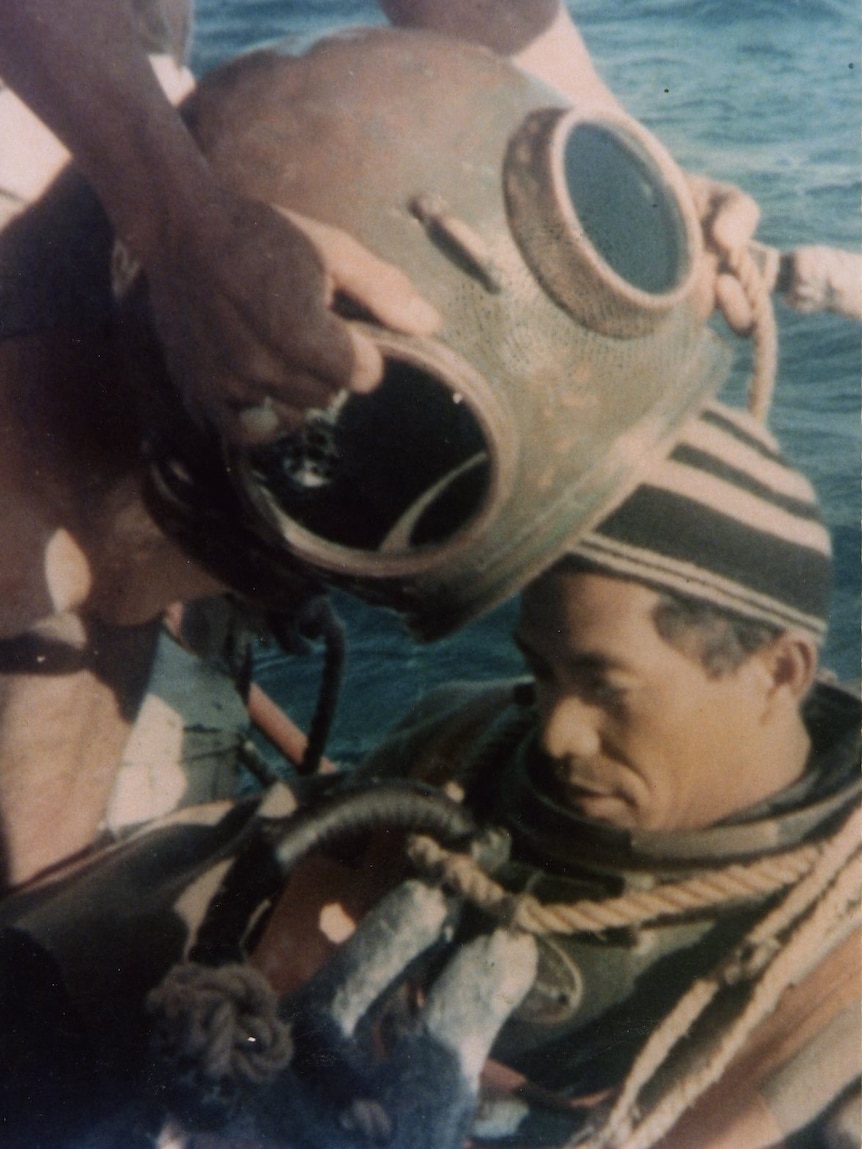 A pearl diver prepares to put on an old diving helmet.