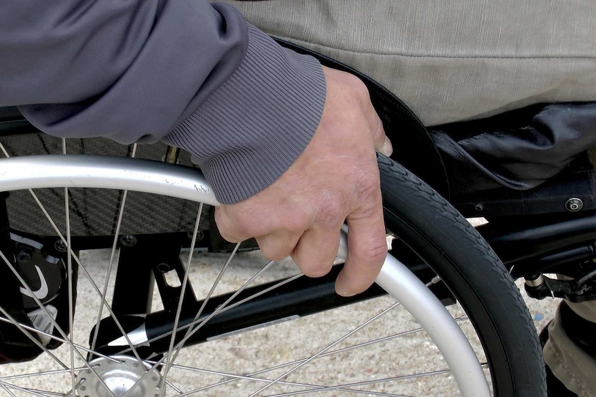 A man's hand on the wheel of a wheelchair
