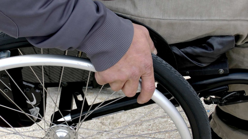 A man's hand on the wheel of a wheelchair