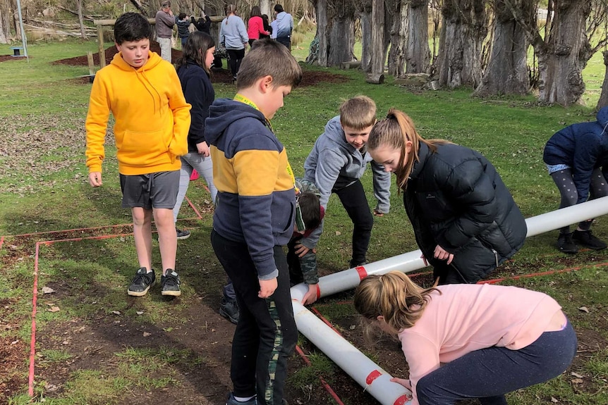 A group of children move balls through a large plastic pipe.