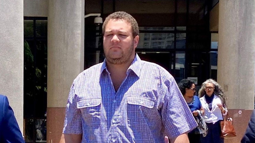 A heavyset man with close-cropped, curly hair and beard stubble walks away from a court building.