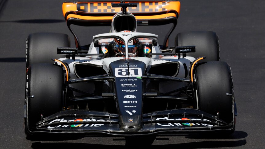 An orange, white and black F1 car is driving down a straight, heading towards the camera, with the driver visible.