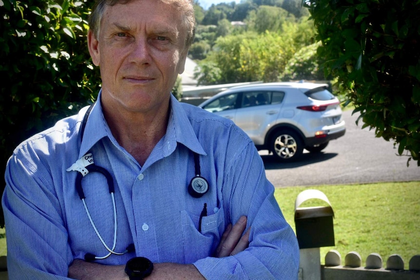 A doctor stands outside with his arms crossed and a stethoscope around his neck.