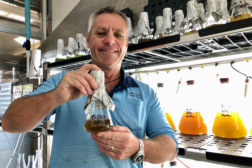 A man holds up a beaker with green algae floating in it.