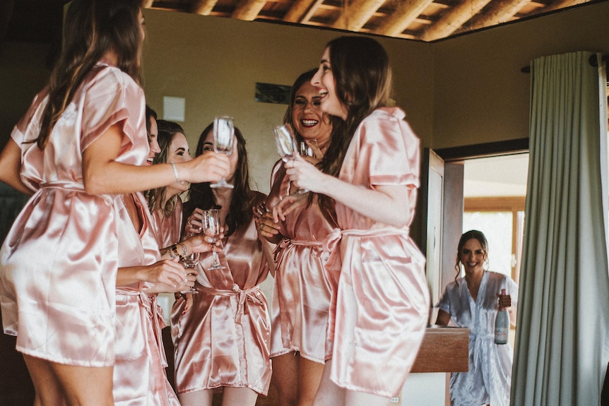 bridesmaids standing on bed together with wine glasses