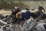 An investigator looks through helicopter wreckage on a hillside.