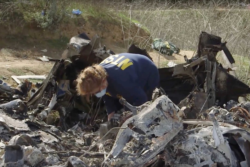 An investigator looks through helicopter wreckage on a hillside.