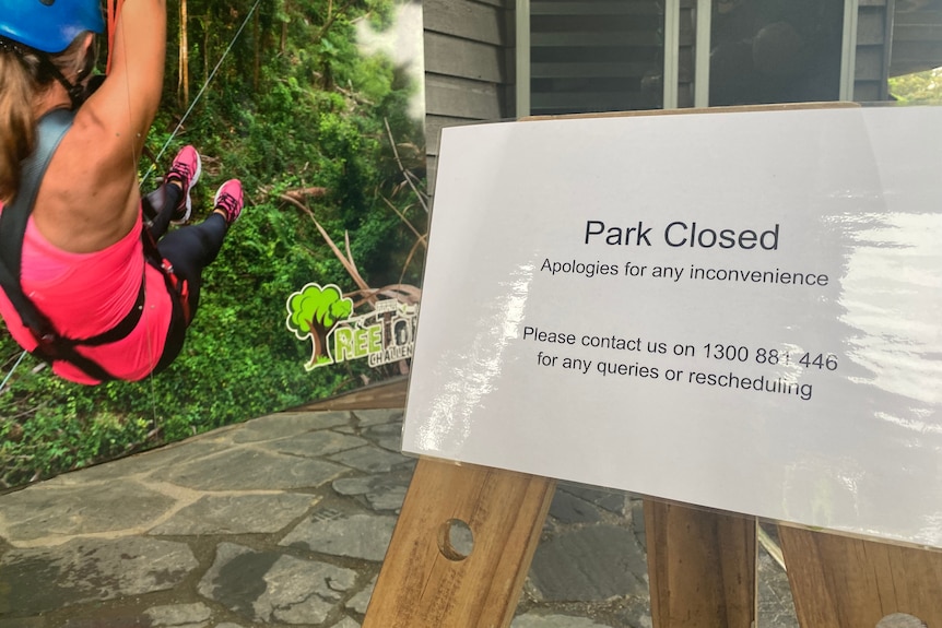 A sign that reads "Park Closed" in on display, with the back of a person in zip-line visible beside it.