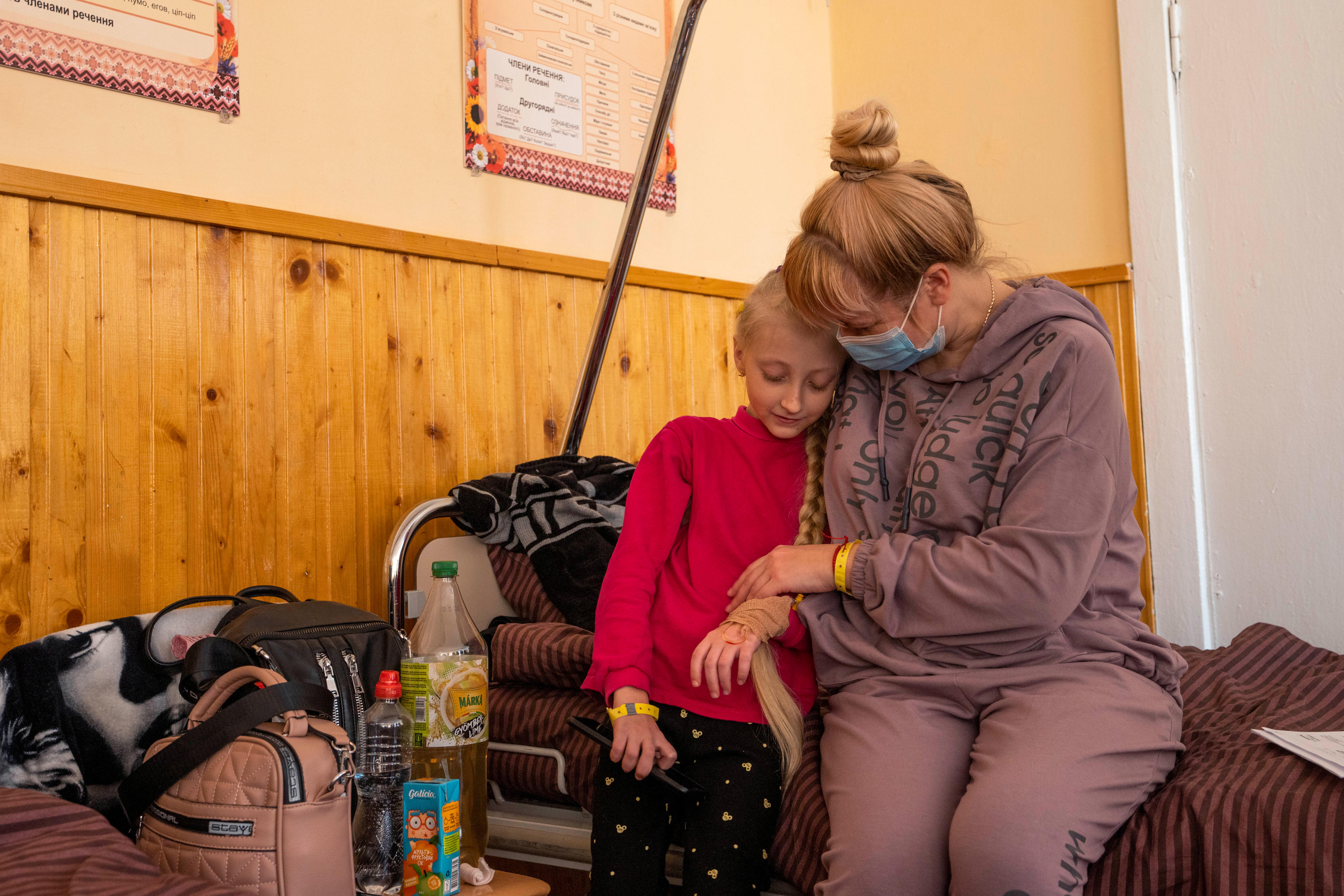 Mother looks down while holding her 10-year-old daughter. Both are sitting on a bed.