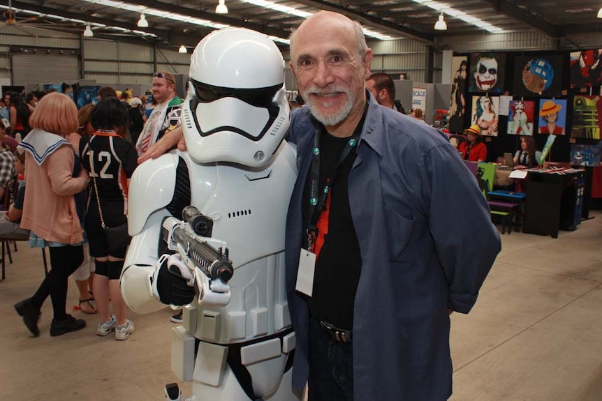 One man in a storm trooper outfit and an older gentleman with a beard smile in front of a crowd.