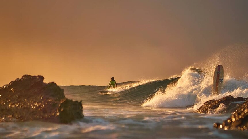 A surfer riding a wave at sunrise.