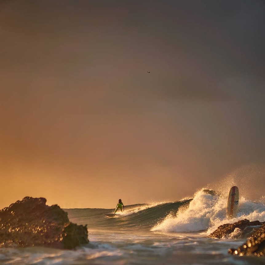 A surfer riding a wave at sunrise.