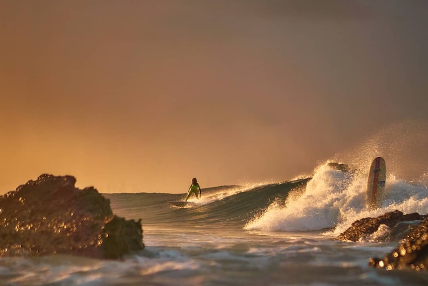A surfer riding a wave at sunrise.
