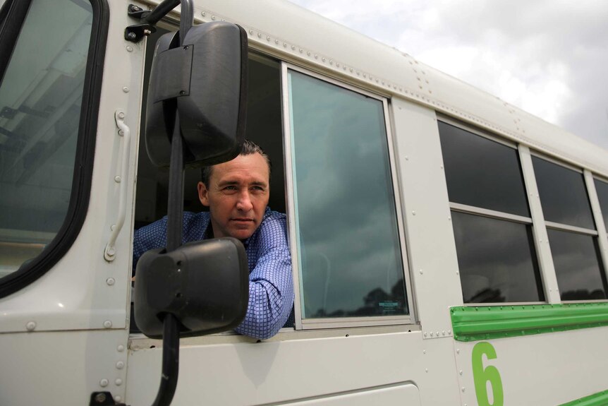 A man leans out the drivers window of a bus.