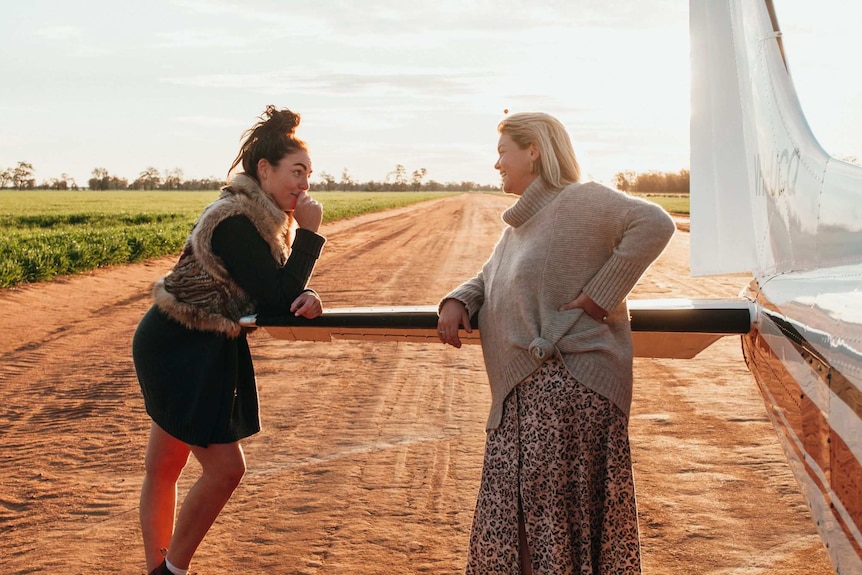 Lucy Taylor and Lucy Samuels lean on back the plane on a dirt runway.