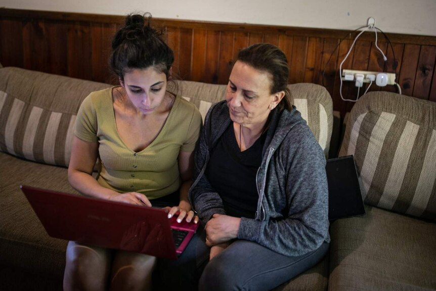 Two women look at a laptop while sitting on a couch