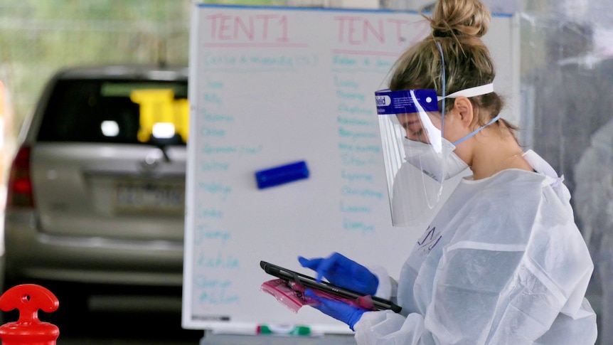 A healthcare worker in PPE looks at a screen while conducting COVID tests.