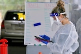 A healthcare worker in PPE looks at a screen while conducting COVID tests.