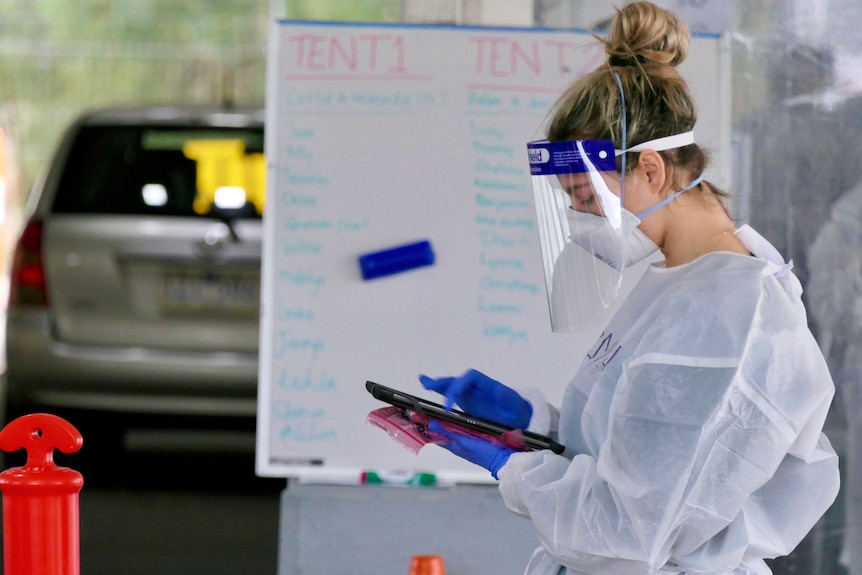 A healthcare worker in PPE looks at a screen while conducting COVID tests.