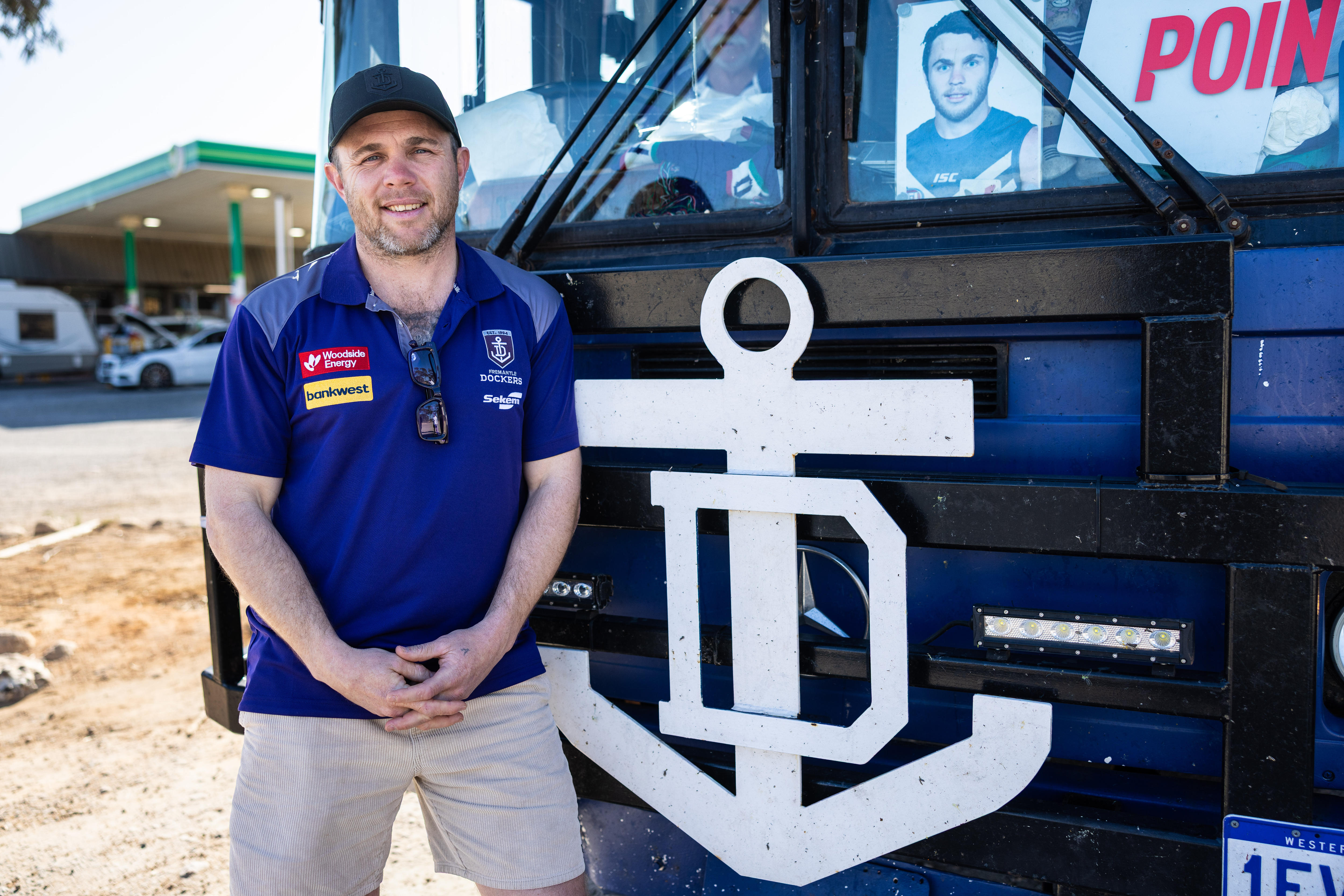 Hayden Ballantyne standing in front of a bus with Fremantle Dockers logo.