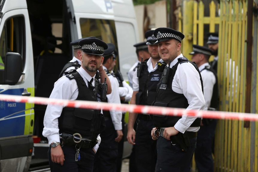 Police officers stand behind a cordon, outside a property which was raided.